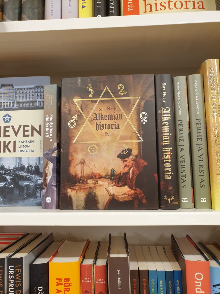 Alkemian historia -kirja kirjahyllyssä muiden kirjojen joukossa.